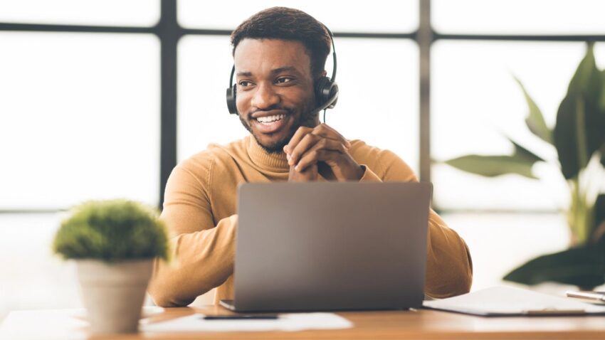 Homme souriant, casque aux oreilles, assis à son bureau devant un ordinateur