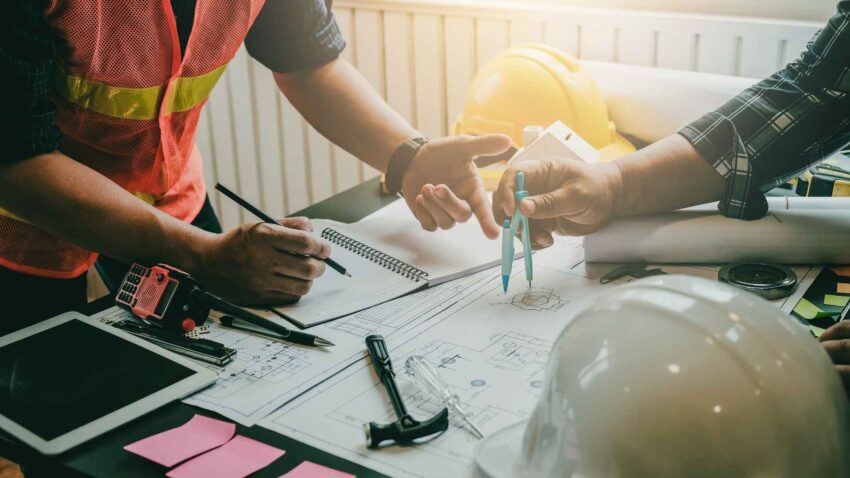 Deux personnes travaillent sur une table avec des plans de construction, des outils et du matériel