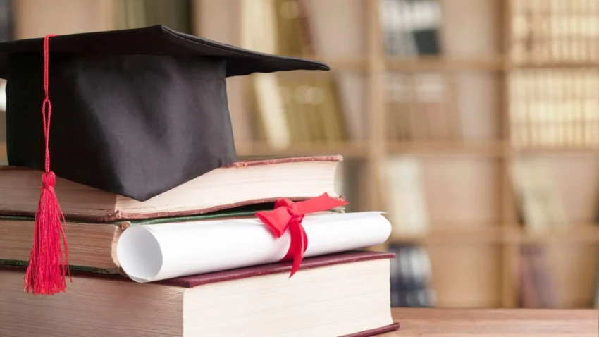 Une pile de trois livres avec un chapeau de diplômé et un diplôme roulé