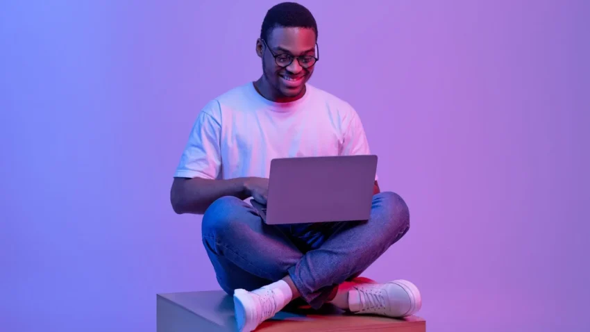 A smiling man sitting and holding his computer