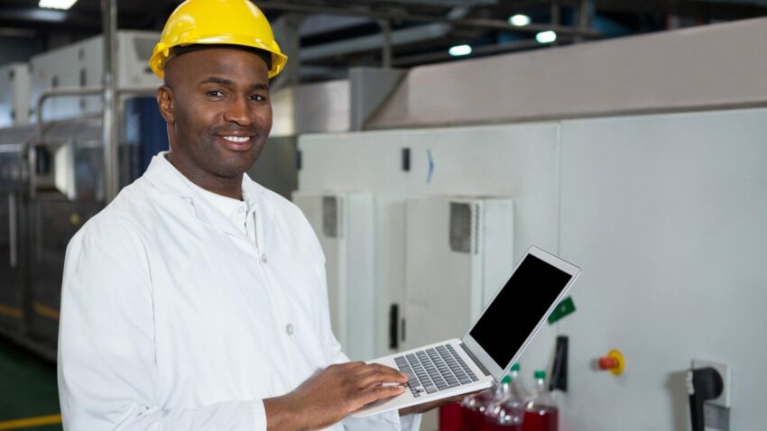 Un technicien en blouse blanche et casque de protection, tenant son ordinateur